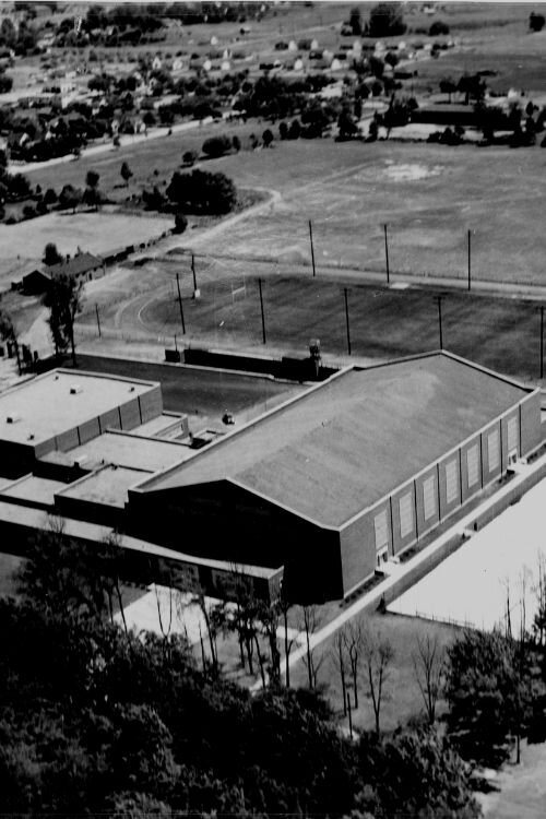 An aerial view of Finch Fieldhouse in 1953 showing the old Alumni Field and outdoor track; the field behind it is the current location of the College of Health Professions and the Medical School.

