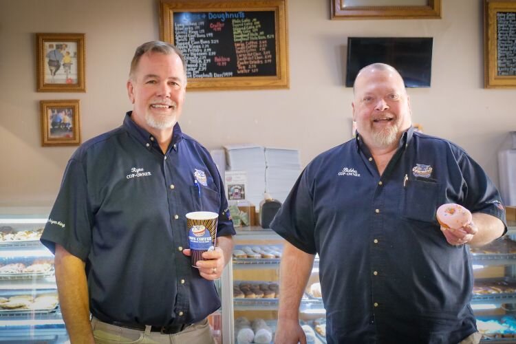 Pictured left to right, Greg “Ryno” Rynearson and Alan “Bubba” White stand side-by-side  amidst the delicious offerings of their beloved Cops & Doughnuts Clare doughnut shop and bakery. Photo Credit: Courtney Jerome / Epicenter Mt. Pleasant 