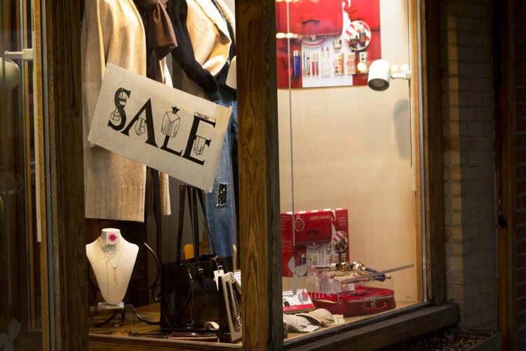 A window display is lit up at night at Trillium Fine Clothing, a women's clothing store that also offers women's accessories such as jewelry and cosmetics.