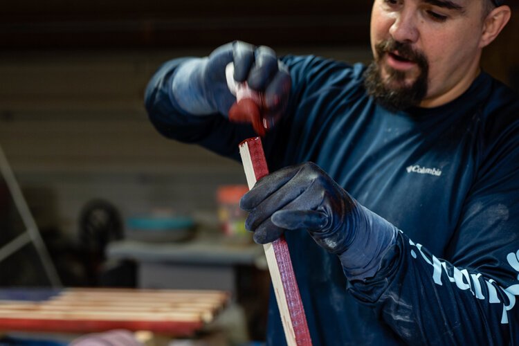 Johnston places red varnish on a piece of wood that will eventually become part of one of his wooden American flags.