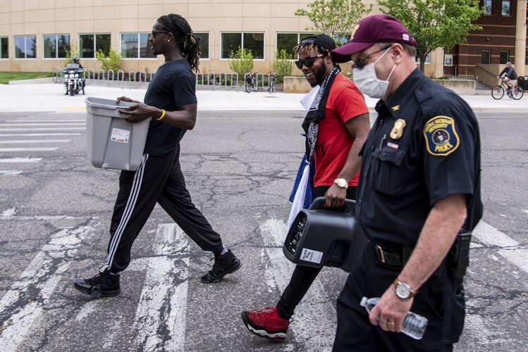 Trokon Jayqua, left, and Tim Crosby, both of Mt. Pleasant, carry equipment to a police officer’s vehicle before an event to protest the death of George Floyd and social injustice June 1 at Central Michigan University.