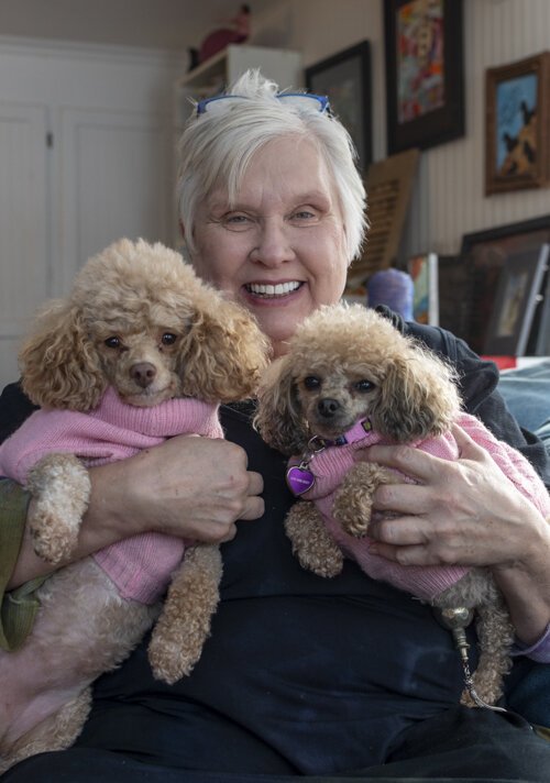 Sue Bergeson sits in her living room, which overlooks Gray Lake, holding her two dogs, Andromeda and Alsyon. 