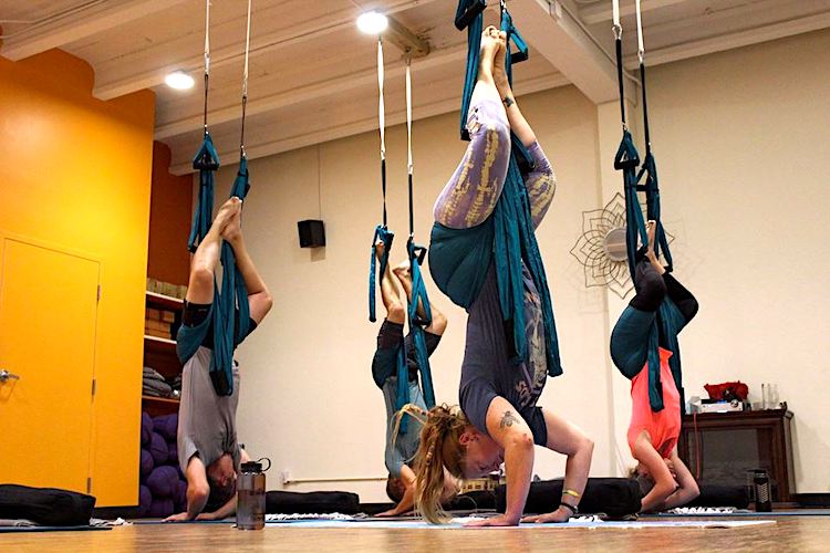 A small group practices inversion during an aerial yoga session at RedBloom Yoga Center in Mt. Pleasant