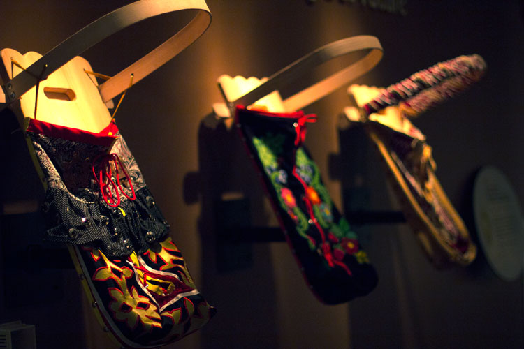 Traditional wood and fabric baby carriers are displayed along a wall in the Ziibiwing Center