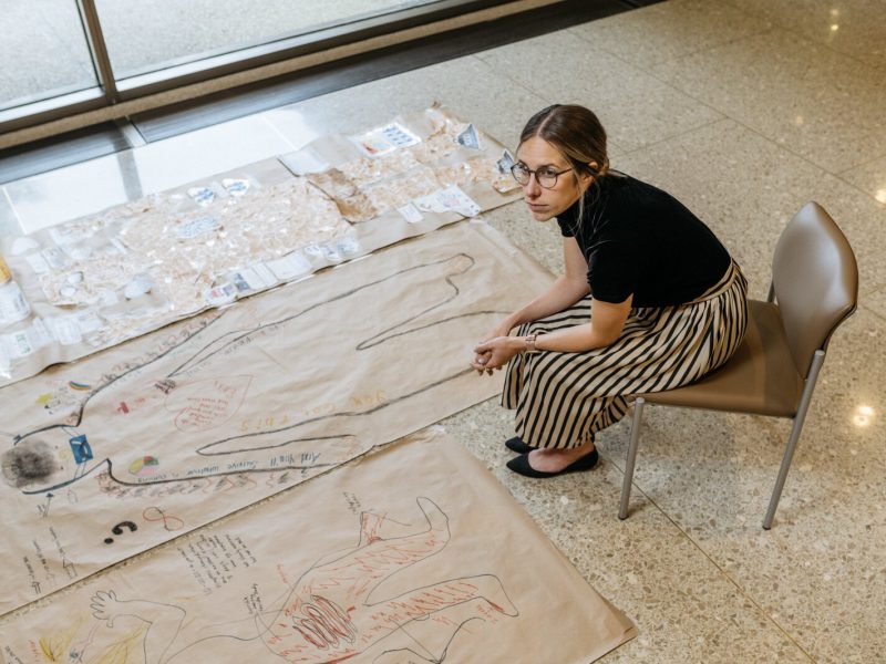 Dr. Sara Santarossa is the lead on a Henry Ford Health project that asked COVID long haulers to draw body maps representing their condition. She sits next to several of their works here.